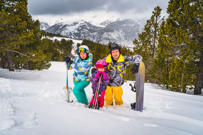 Family standing in deep snow and holding ski and snowboard. winter holidays in andorra