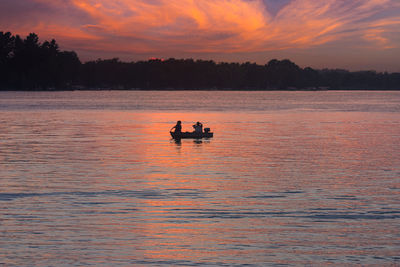 Silhouette people on boat in sea against orange sky