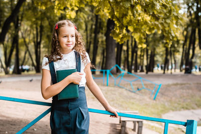 A pupil in a school uniform with a book walks on a warm day in the park