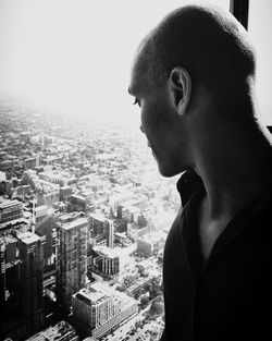 Young man looking towards buildings in city through apartment window