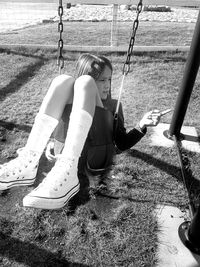 High angle view of girl pointing while sitting on swing in playground