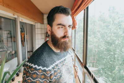Portrait of young man standing against window