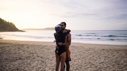 Young couple standing on beach against sky