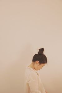 Side view of young woman standing by white wall