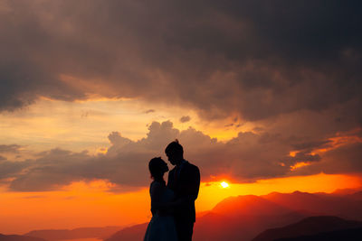 Silhouette couple standing against orange sky