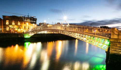 Illuminated bridge over river in city against sky at night