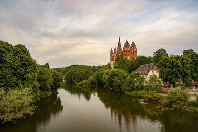 Reflection of building and trees on river against sky