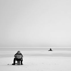 Rear view of man sitting on beach against clear sky