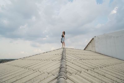 Low angle view of woman standing on roof against cloudy sky