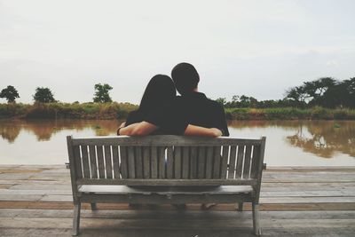 Rear view of couple sitting on lake against sky