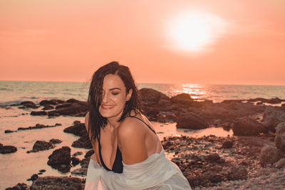 Smiling woman sitting at beach against clear sky during sunset