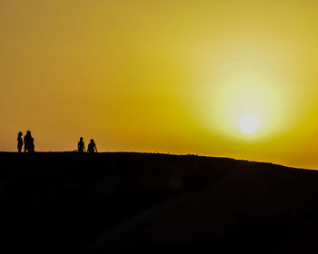 Silhouette people on street against sky during sunset