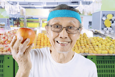 Portrait of smiling senior man holding apple in supermarket