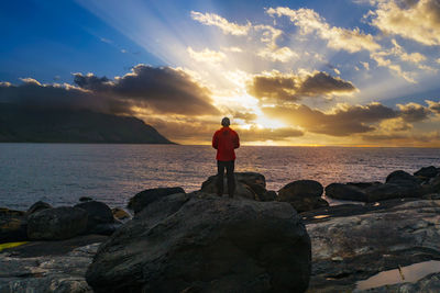 Rear view of woman standing at beach against sky during sunset