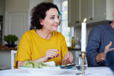 Smiling mature woman looking away while sitting by friend at dining table