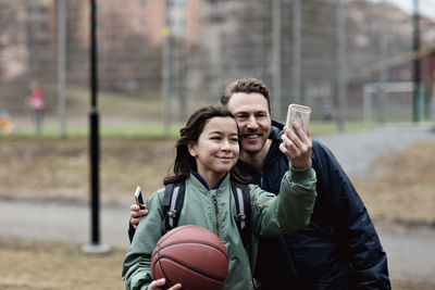 Smiling son taking selfie with father after basketball practice in winter