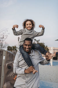 Joyful son sitting on happy father's shoulders at park playground