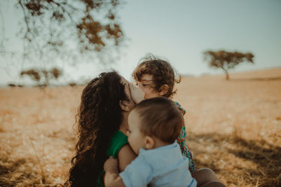 Mother and cute kids sitting on field against sky