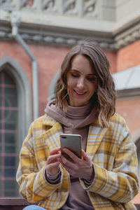 Happy millenial woman in a yellow coat in european city near historic building.