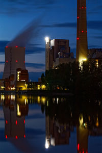 Illuminated buildings by river against sky at dusk