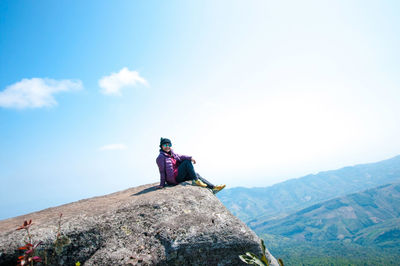 Full length of woman sitting on cliff against sky