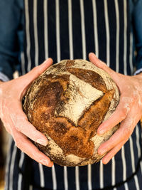 A man in stripped blue apron is holding freshly baked sourdough bread. traditional french loaf.