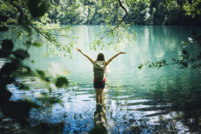 Woman looking at lake levico standing with arms outstretched on tree log