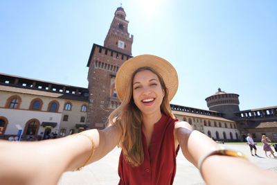 Beautiful happy tourist woman takes selfie by camera in milan, italy