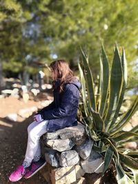 Side view of girl sitting on rocks at field