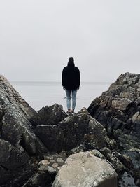 Rear view of man standing on rock by sea against sky
