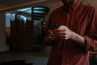 Midsection of man using mobile phone while standing at home