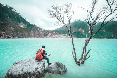 Rear view of man sitting on shore against sky