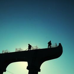 Low angle view of silhouette people on bridge against clear sky