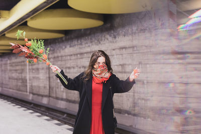 Woman holding bouquet with scarf covering face standing on footpath