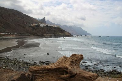 Scenic view of sea by mountain against sky