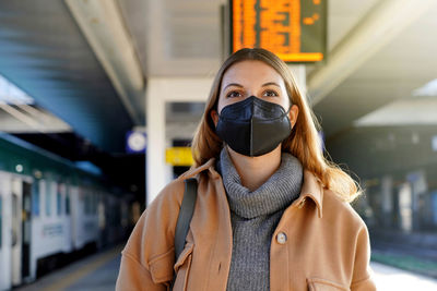 Beautiful woman wearing black face mask ffp2 kn95 in train station with timetables on background