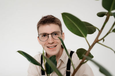 Close-up portrait of smiling young man with plant against white background