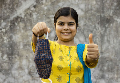 Indian woman in yellow dress holding homemade cotton mask and showing thumb-up as like gesture