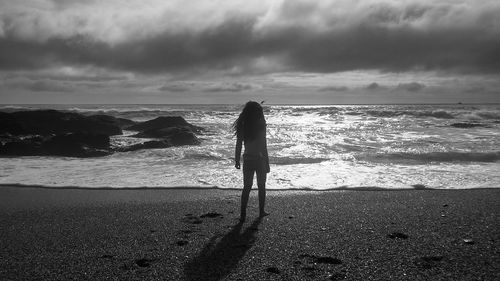 Woman standing on beach against cloudy sky