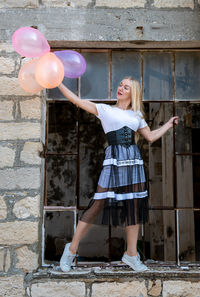 Happy woman having fun holding colorful air balloons on a broken window