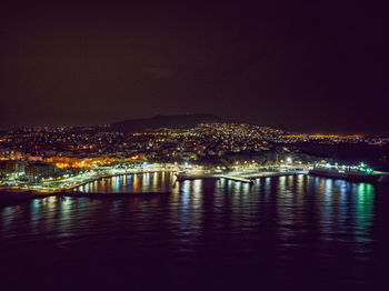 Illuminated buildings by river against sky at night