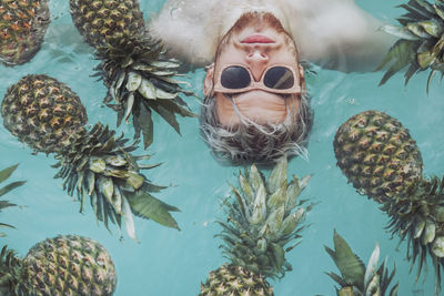 Young man in swiming pool surrounded by pineapples