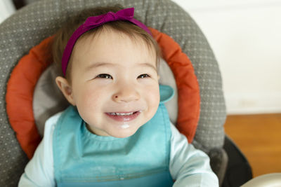 Adorable smiling baby girl wearing headband sits in highchair at home