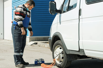 Side view of man standing by car on road