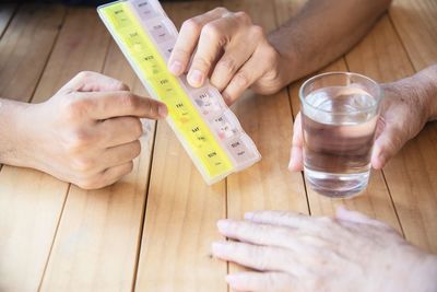 Close-up of hand holding glass of water by person with pill box on table