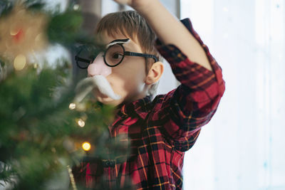 Little cute caucasian boy decorating christmas tree with twinkling decorations.