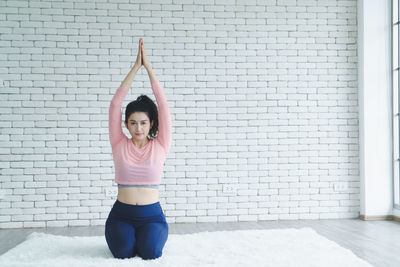 Full length of woman with arms raised against brick wall