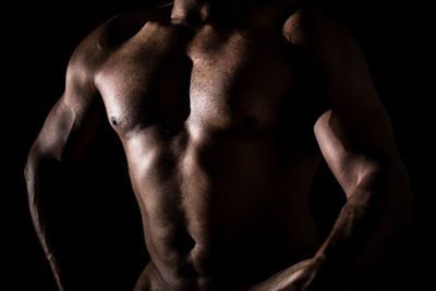 Midsection of shirtless man standing against black background