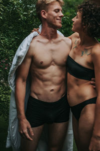 Midsection of shirtless young man standing against plants