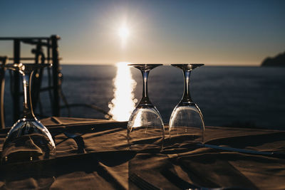 Wine glass on table by sea against sky during sunset